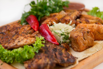 Meat dish. Pieces of roasted meat, parsley, sauce, red pepper, lettuce leaves lie on a wooden board. Isolated on white background