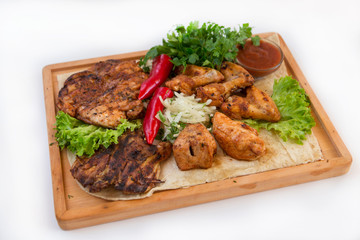 Meat dish. Pieces of roasted meat, parsley, sauce, red pepper, lettuce leaves lie on a wooden board. Isolated on white background