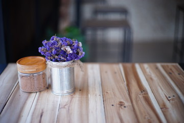purple flower in aluminium pot and brown sugar in glass on wood table at cafe.