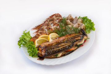 Fish dish. Fried and baked fish, parsley, lettuce leaves and lemon lie on a white plate. Isolated on white background
