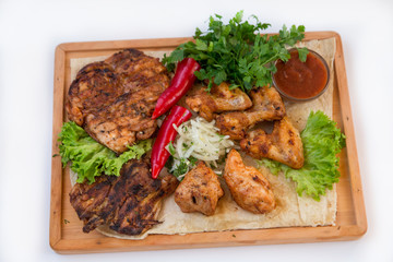 Meat dish. Pieces of roasted meat, parsley, sauce, red pepper, lettuce leaves lie on a wooden board. Isolated on white background