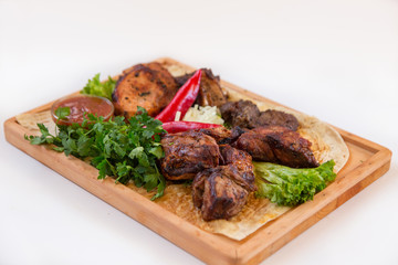 Meat dish. Pieces of roasted meat, parsley, sauce, red pepper, lettuce leaves lie on a wooden board. Isolated on white background