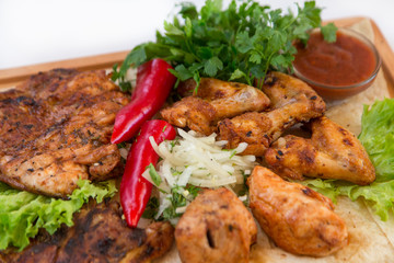 Meat dish. Pieces of roasted meat, parsley, sauce, red pepper, lettuce leaves lie on a wooden board. Isolated on white background