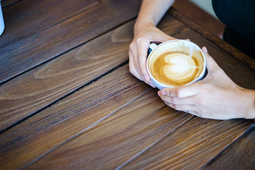 latte art coffee with hand on wood table in cafe.