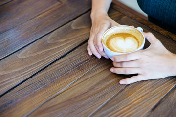 latte art coffee with hand on wood table in cafe.