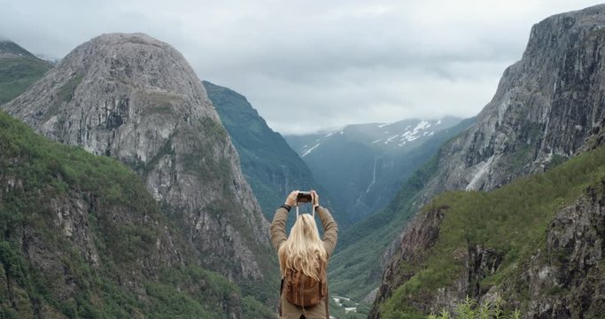 Backpacker Woman taking photograph glacier valley smartphone wearing backpack photographing scenic landscape nature background view enjoying vacation travel adventure Norway