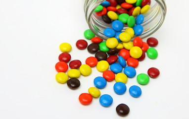 Colorful sugar-coated chocolate smarties in a glass jar on a white background
