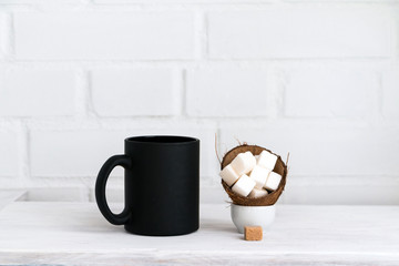 Black mug and sugar cubes on white table against white brick wall. Copy space.