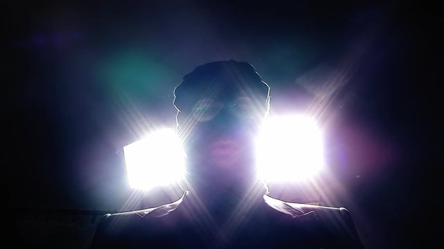 A terrorist with a balaclava over his face, recording a message in which he is menacing us (victim's point-of-view). Strong lights behind him. Close-up shot.
