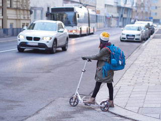 Gefahrenzone - Kind wartet mit Scooter am Fahrbahnrand