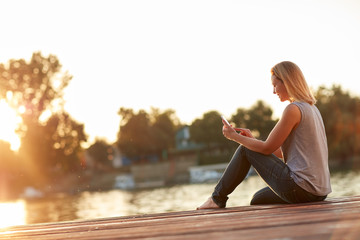 Lady with phone enjoying at sunset on the river