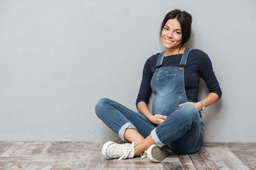 Cheerful pregnant lady sitting on floor