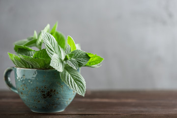 Twigs of mint in a cup on a wooden table in soft focus with copy space
