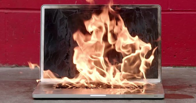 Person setting laptop computer on fire with match