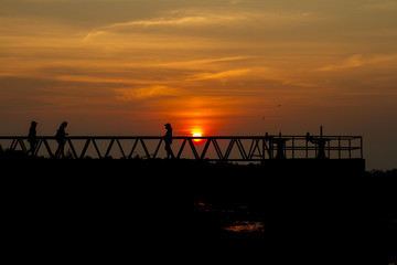 silhouette of people standing on a bridge at sunset.