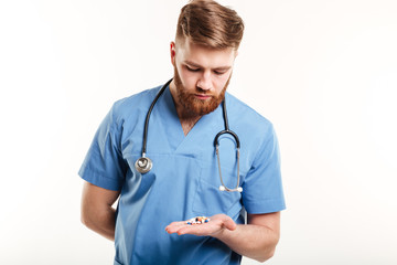 Doctor or nurse with stethoscope looking at pills in palm