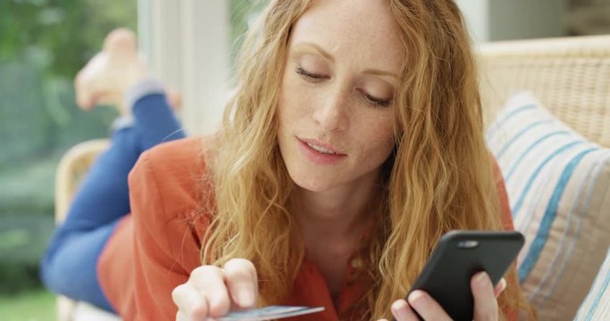 Online shopping Close up of beautiful red haired woman holding credit card making payment using smartphone at home in trendy loft apartment 