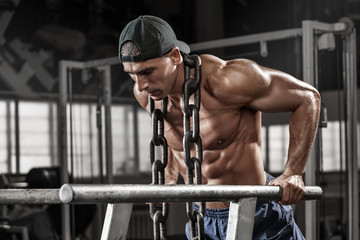 Muscular man working out in gym doing exercises on parallel bars with chain, strong male naked...
