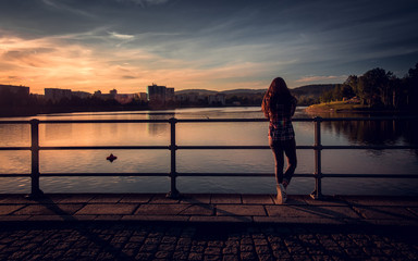 Fototapeta premium Girl standing by the lake dam in the sunset, Jablonec nad Nisou, Czech republic