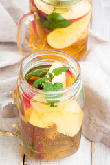 Cold tea with red apple, mint and cinnamon stick in a glass jar on a white background.