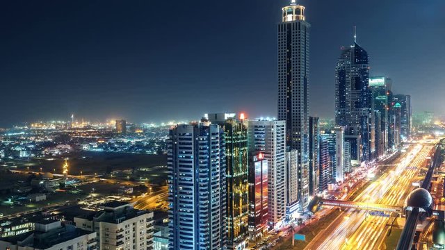 Spectacular nighttime skyline of Dubai. UAE. Top view of business bay skyscrapers, highway with light trails and metro station.4K time lapse. Colourful travel background.