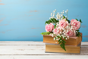 Naklejka premium Rose flower bouquet on old books over wooden background with copy space