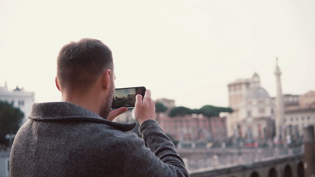 Handsome man with a beard exploring new city, taking photos of city on smartphone. Guy have vacation in Rome, Italy.