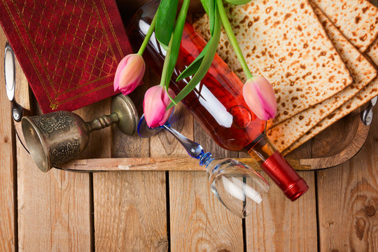 Jewish holiday Passover Pesah celebration with matzoh, tulip flowers and wine bottle on wooden background. View from above