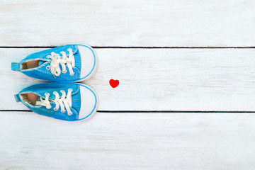 Blue sneakers for a boy and a red heart on a white wooden background. view from above