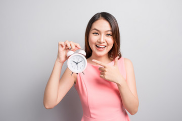 Pretty asian girl with surprised face holding an alarm clock in her hand and looking at it with opened mouth