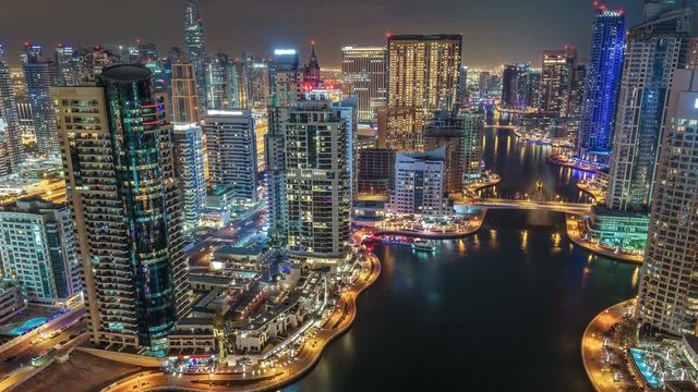 Colourful skyline of Dubai Marina by night. Scenic aerial view over the creek with skyscrapers, roads and sailing boats. 4K time lapse. Famous travel destination.