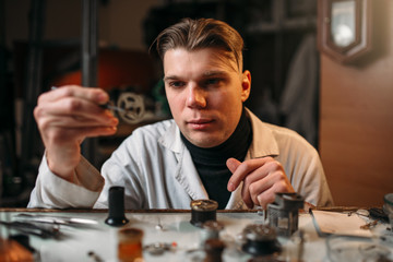 Watchmaker holding with tweezers a gear of hours