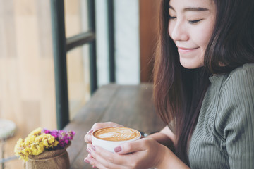 Closeup image of a beautiful Asian woman holding and drinking hot coffee with feeling good in wooden vintage cafe