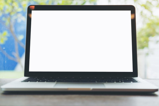 Mockup image of laptop with blank white screen on wooden table with blue sky and nature background through a mirror window