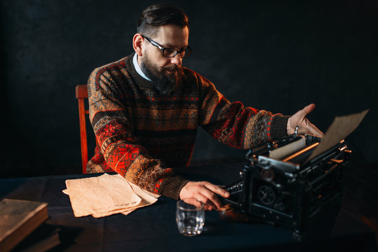 Bearded poet in glasses typing on typewriter