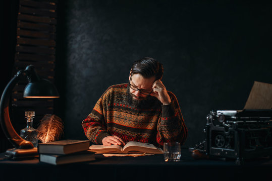 Bearded author in glasses reading a book