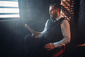Bearded writer in glasses reads handwritten text - obrazy, fototapety, plakaty