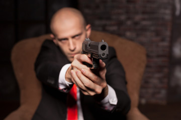Bald killer in suit and red tie aims a pistol