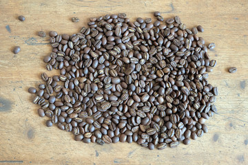 Lot of scattered roasted coffee beans on an old wooden table top view