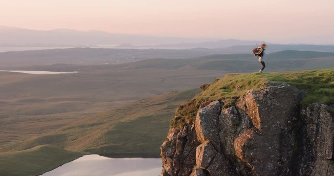 Woman dancing silly freestyle dance outdoors standing on cliff edge at sunrise Crazy dancer girl having fun enjoying nature celebrating vacation travel adventure Scotland