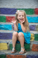 small happy baby girl in blue dress on colorful stairs