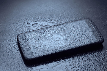 Wet smartphone with water drops on dark blue background