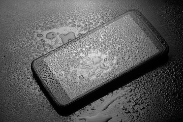 Wet smartphone with water drops on dark background