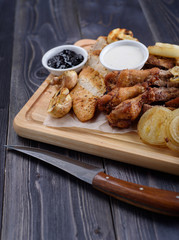 Fried meat slices of chicken wings, ham, fillets with sauce on a wooden board