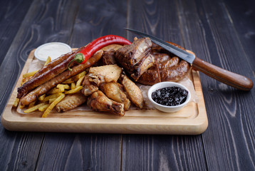 Grilled sausages and chicken with fries on a wooden board
