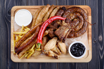 Grilled sausages and chicken with fries on a wooden board