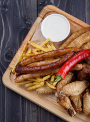 Grilled sausages and chicken with fries on a wooden board