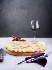 Pizza bianca with chicken, ham and cream sauce on a wooden board next to a glass of wine, grapes and pieces of cheese