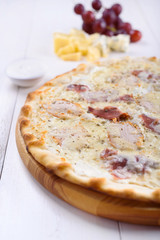 Pizza bianca with chicken, ham and cream sauce on a wooden board next to a glass of wine, grapes and pieces of cheese