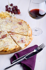 Pizza bianca with chicken, ham and cream sauce on a wooden board next to a glass of wine, grapes and pieces of cheese